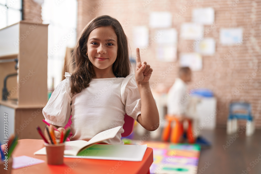 Little hispanic girl painting at the school smiling with an idea or question pointing finger with happy face, number one Little hispanic girl painting at the school smiling with an idea or question pointing finger with happy face, number one
