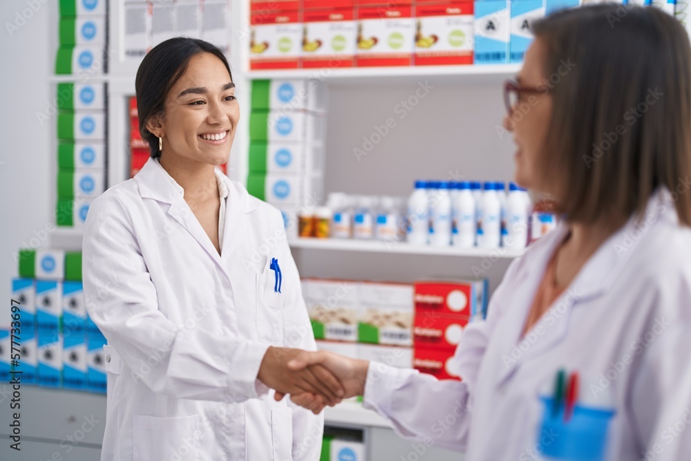 Two women pharmacist smiling confident shake hands at pharmacy