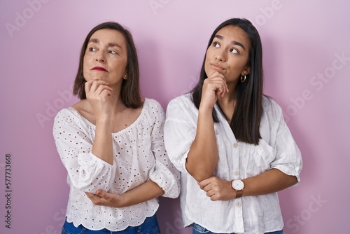 Hispanic mother and daughter together with hand on chin thinking about question, pensive expression. smiling with thoughtful face. doubt concept.