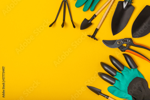 Gardening tools on a yellow background in a greenhouse. Spring in the garden. Garden shovels and rakes, secateurs, gloves for gardening on a bright background. Flat lay. Gardening and hobby concept.