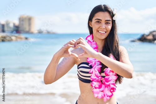 Young brunette woman wearing bikini at the beach smiling in love doing heart symbol shape with hands. romantic concept.