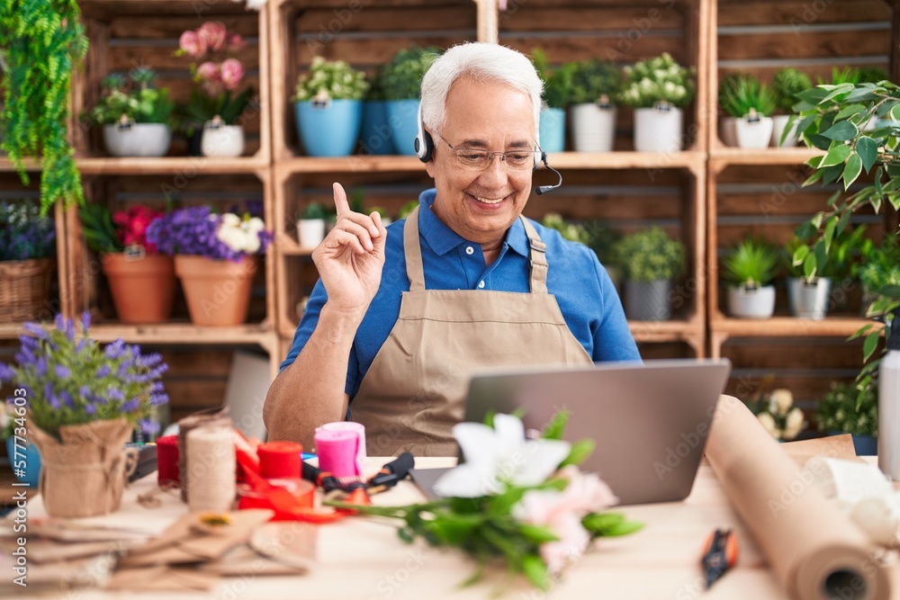 Middle age man with grey hair working at florist shop doing video call smiling happy pointing with hand and finger to the side Middle age man with grey hair working at florist shop doing video call smiling happy pointing with hand and finger to the side