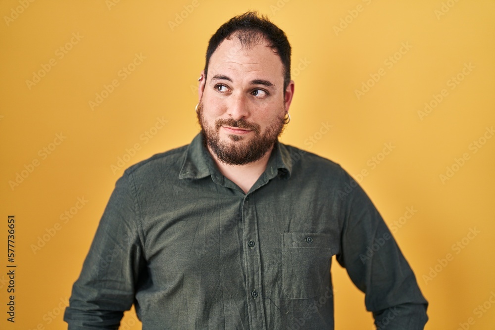 Plus size hispanic man with beard standing over yellow background smiling looking to the side and staring away thinking. Plus size hispanic man with beard standing over yellow background smiling looking to the side and staring away thinking.