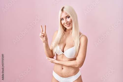Caucasian woman wearing lingerie over pink background smiling with happy face winking at the camera doing victory sign. number two.