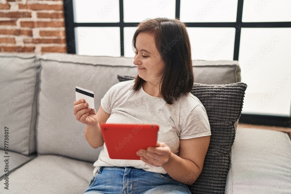 Down syndrome woman using touchpad and credit card sitting on sofa at home Down syndrome woman using touchpad and credit card sitting on sofa at home