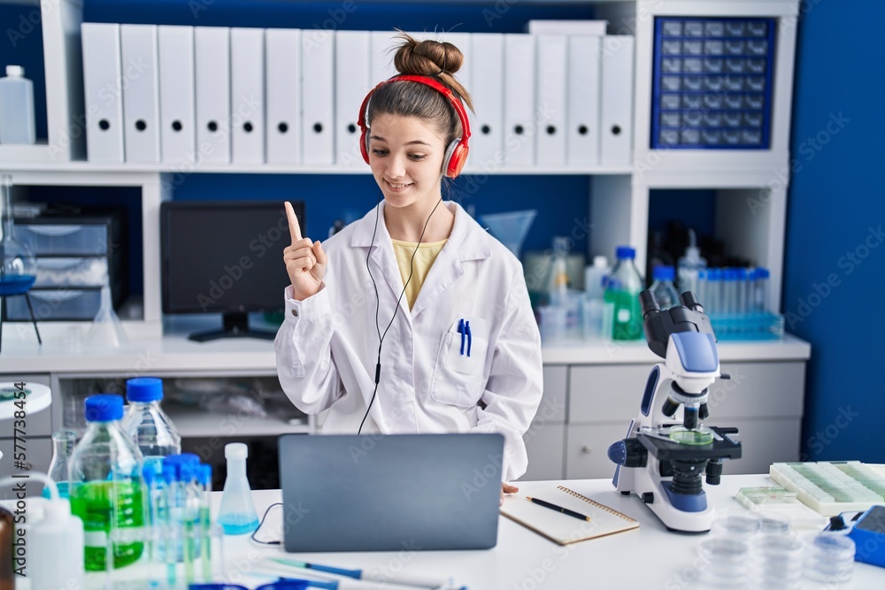 Teenager girl working at scientist laboratory smiling with an idea or question pointing finger with happy face, number one