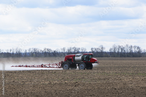 Red tractor with irrigation system watering a field on a cloudy day. agricultural machinery, work in the field. seasonal work. tractor fertilizes the ground. rides in the field, small tractor