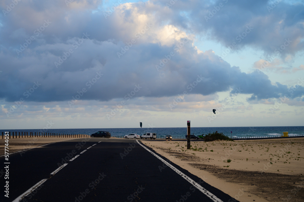 Driving car on black asphalt road through white sandy dunes near Corallejo beach on sunset Fuerteventura, Canary islands, Spain