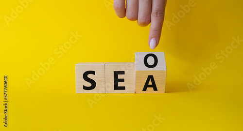 SEO vs SEA symbol. Businessman hand points at cubes with words SEA vs SEO. Beautiful yellow background. Business and SEO vs SEA concept. Copy space