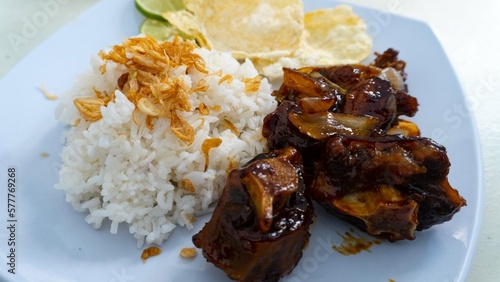 isolated oxtail soup with rice or sup buntut is a popular dish or cuisine in Indonesia made from mainly white rice with half fried beef ribs. In this picture, the dishes were put over a white table  photo