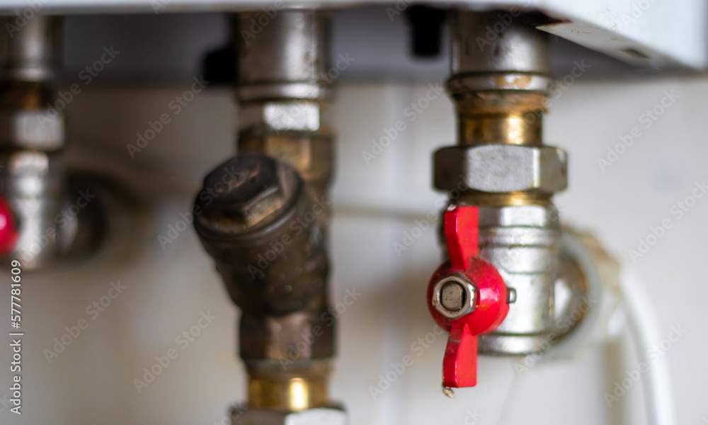 Hidden water taps for connecting a gas boiler on a tiled wall. Plumbing connections for a domestic double-circuit gas boiler. Pipes of the heating system. Installing a gas boiler with red taps. Hidden water taps for connecting a gas boiler on a tiled wall. Plumbing connections for a domestic double-circuit gas boiler. Pipes of the heating system. Installing a gas boiler with red taps.