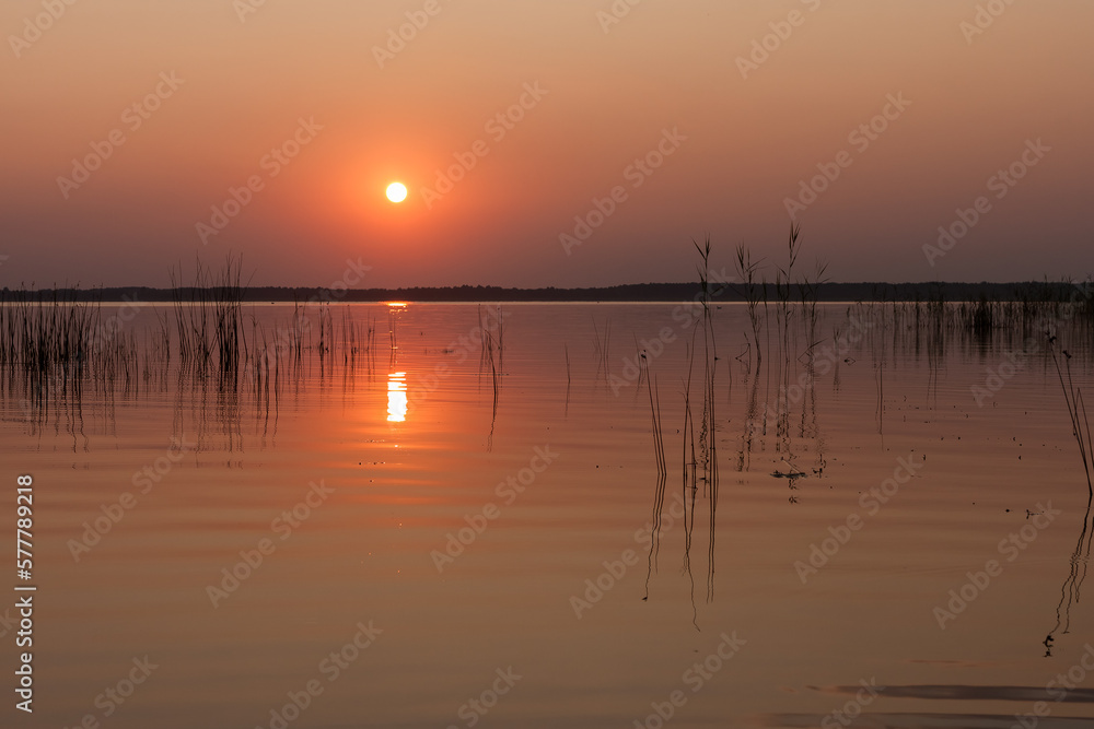 Sunset on the lake. Evening sky with beautiful clouds is reflected in the water of the lake