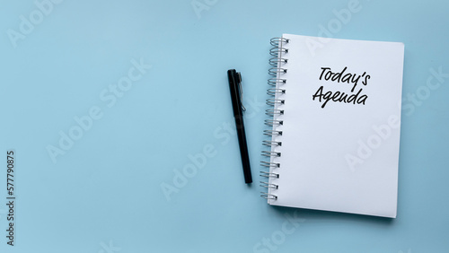 Top view of pen and notebook written with Today's Agenda on blue background with copy space.