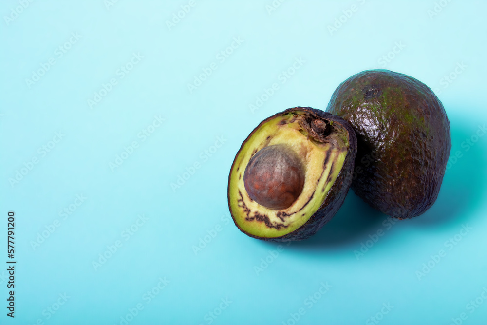 Rotten avocado, overriped, bad avocado. Half sliced fruit, freegan food concept, blue background