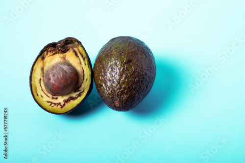 Rotten avocado, overriped, bad avocado. Half sliced fruit, freegan food concept, blue background. The theme of careful consumption and care for the environment. Copyspace