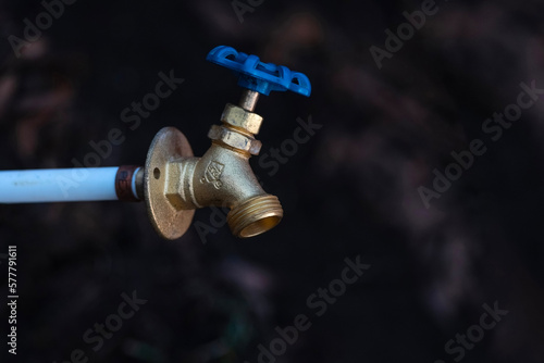 Closeup of a faucet with water drop on dark background with copy space.