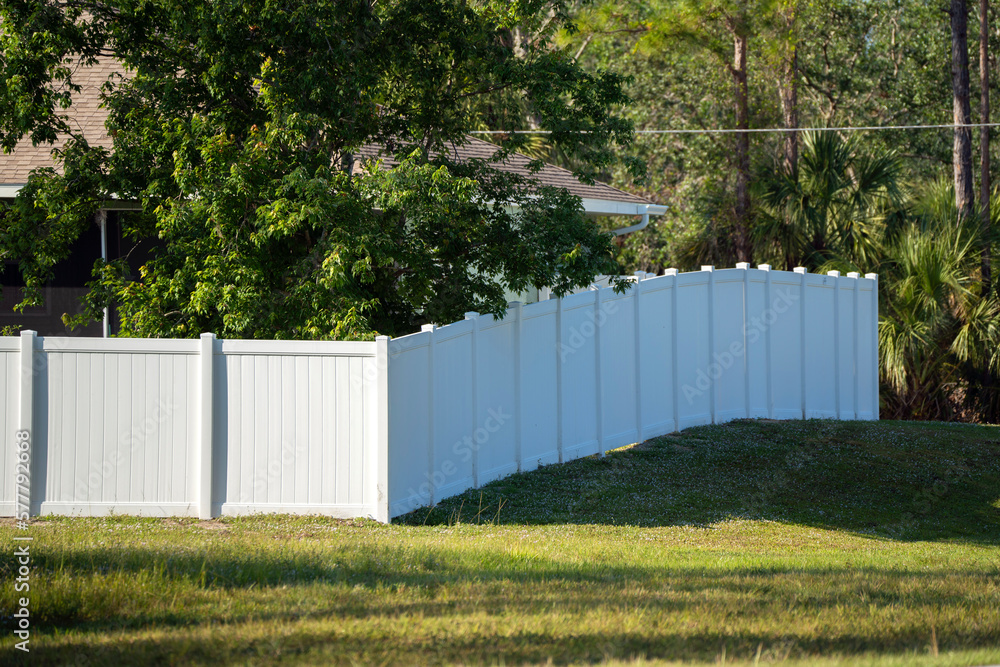 White vinyl picket fence on green lawn surrounding property grounds for backyard protection and privacy White vinyl picket fence on green lawn surrounding property grounds for backyard protection and privacy