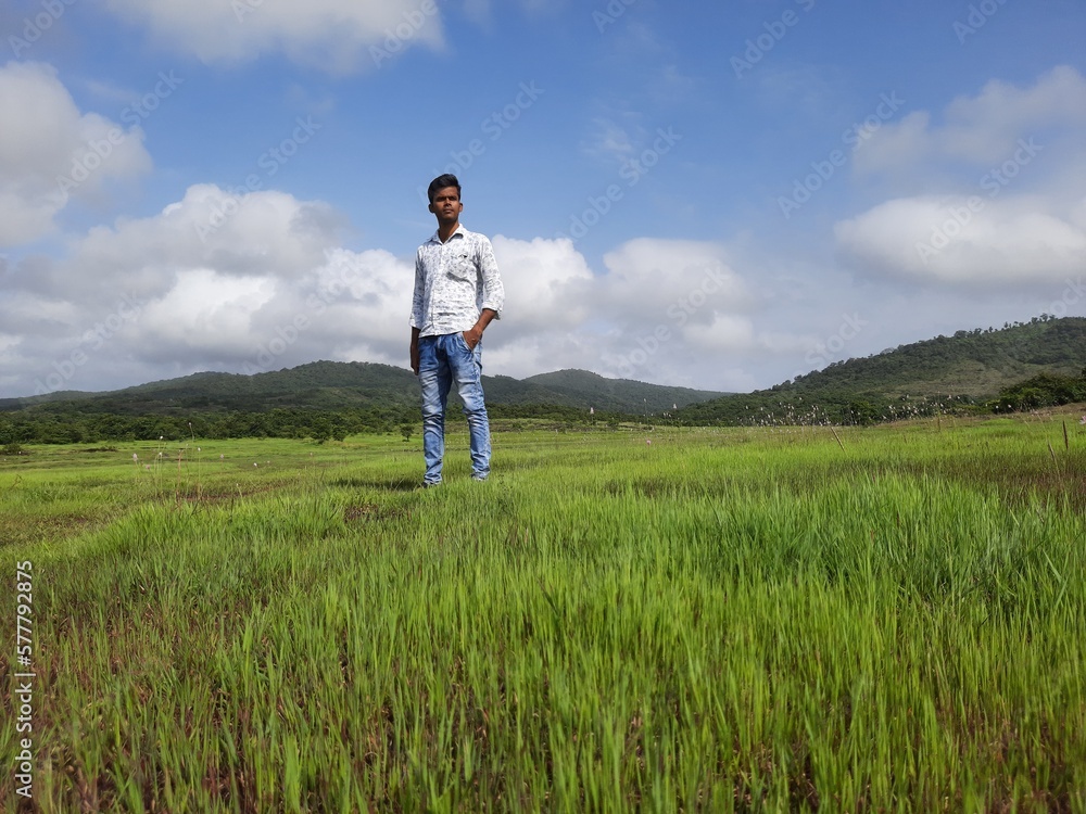 young man standing on the green grass field with blue sky. person on the meadow.