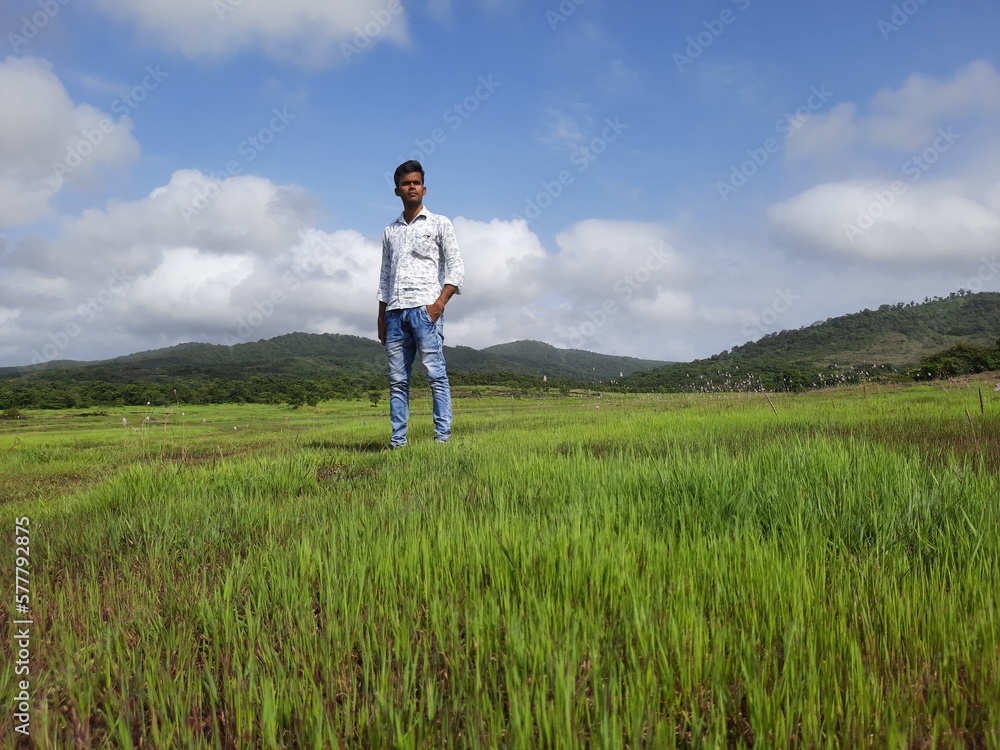 young man standing on the green grass field with blue sky. person on the meadow. young man standing on the green grass field with blue sky. person on the meadow.