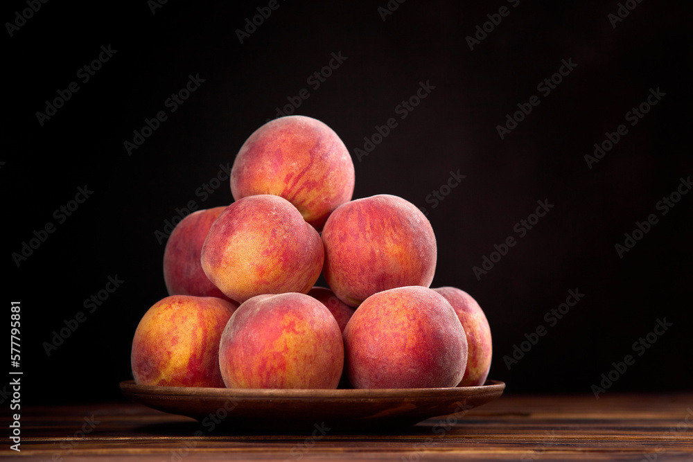 Red-yellow peaches on clay plate on a rustic wooden table against dark background Red-yellow peaches on clay plate on a rustic wooden table against dark background