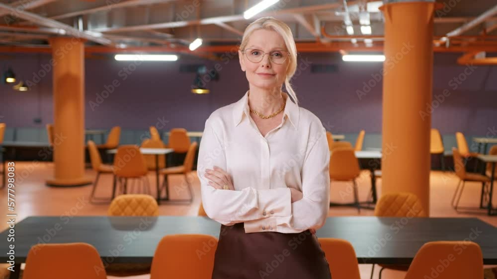 Smart confident mature CEO woman in eyeglasses posing crossing arms at empty business office space background alone after hours. Successful strong businesswoman 50s corporate manager lady boss 4K Smart confident mature CEO woman in eyeglasses posing crossing arms at empty business office space background alone after hours. Successful strong businesswoman 50s corporate manager lady boss 4K