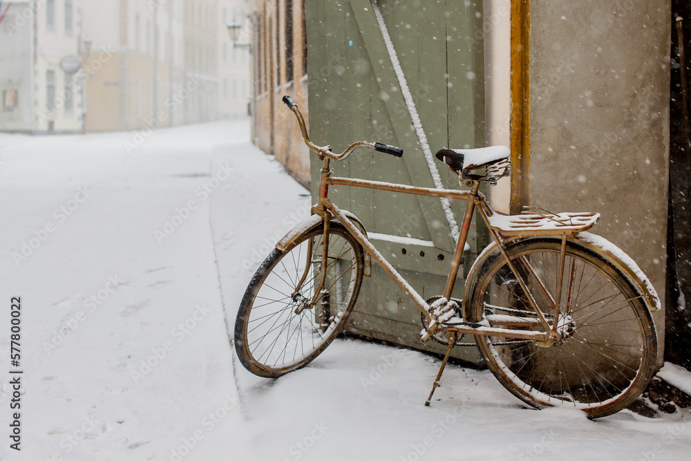 Brown vintage metal bike parked in old town Riga during snow fall covered by snow flakes in winter