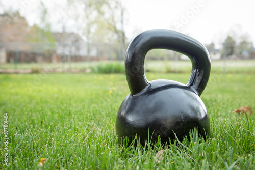 heavy iron black kettlebell on green grass in backyard - outdoor fitness concept
