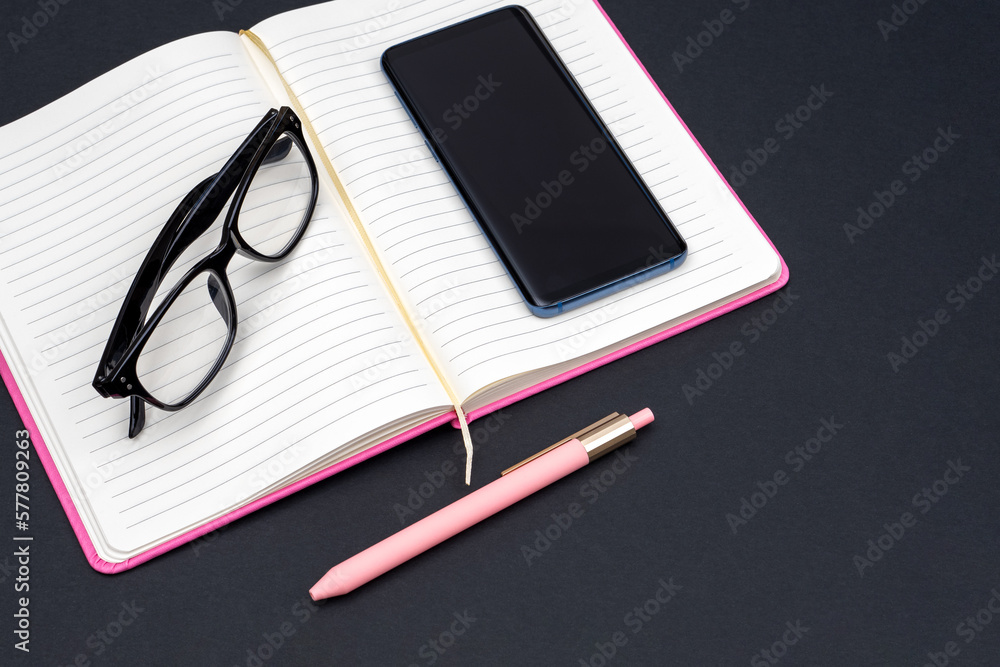 An open diary, reading glasses and a mobile phone, a pen as a concept of reading and planning a working day, household spending, retirement savings An open diary, reading glasses and a mobile phone, a pen as a concept of reading and planning a working day, household spending, retirement savings