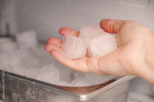 The girl takes frozen ice cubes from the freezer with her hand to prepare soft drinks. photo