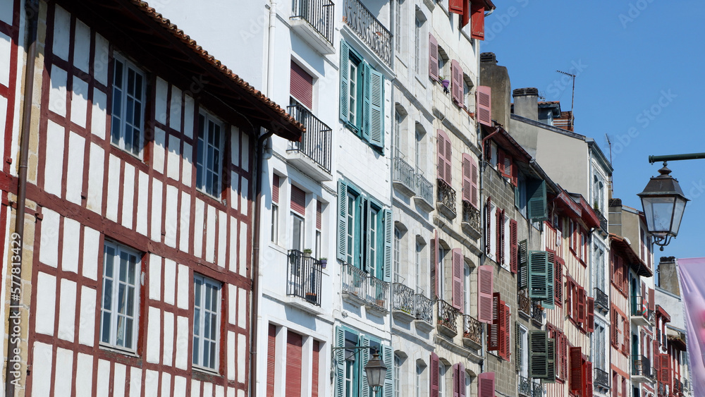 Naklejka premium Colourful vintage facades of typical french basque homes with shutters and windows of faded colours downtown in Bayonne, Basque country, Spain. Panoramic view