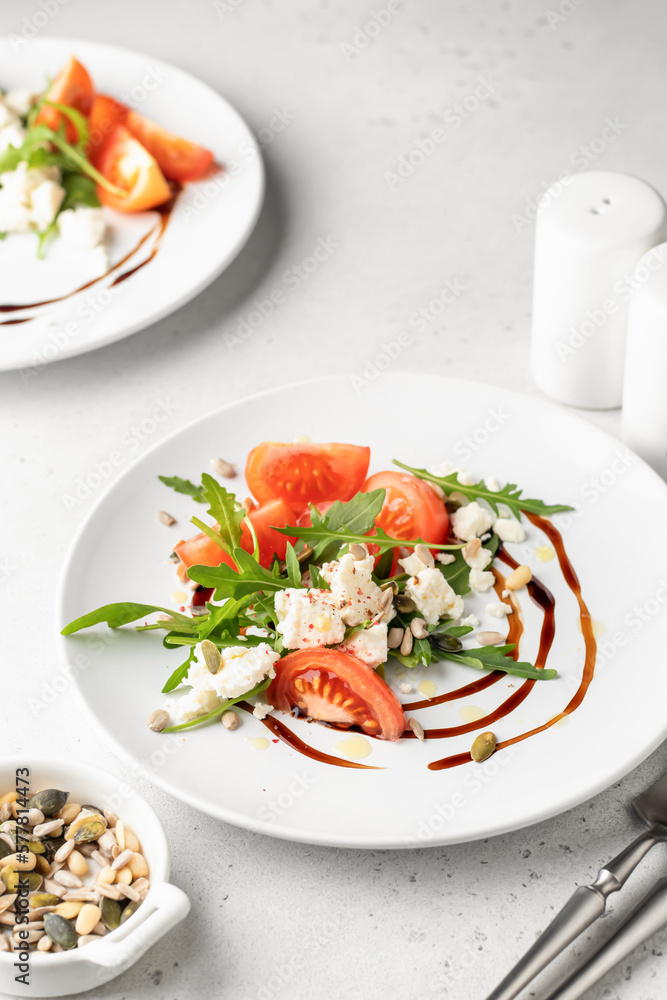 Green salad with arugula, cherry tomatoes, seeds and feta cheese with cutlery on white background. Healthy diet vegetarian salad concept Green salad with arugula, cherry tomatoes, seeds and feta cheese with cutlery on white background. Healthy diet vegetarian salad concept