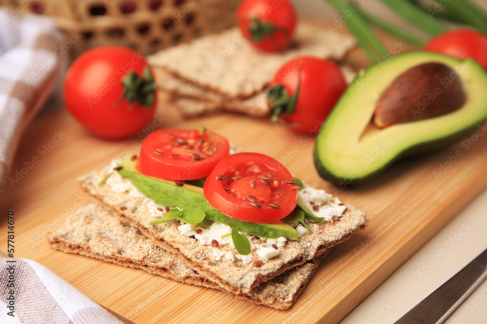 Tasty crispbreads with cream cheese, fresh tomatoes and avocado on beige table, closeup. Space for text