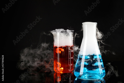 Laboratory glassware with colorful liquids and steam on black background. Chemical reaction