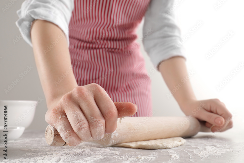 Woman rolling fresh dough at light grey table, closeup. Cooking grissini