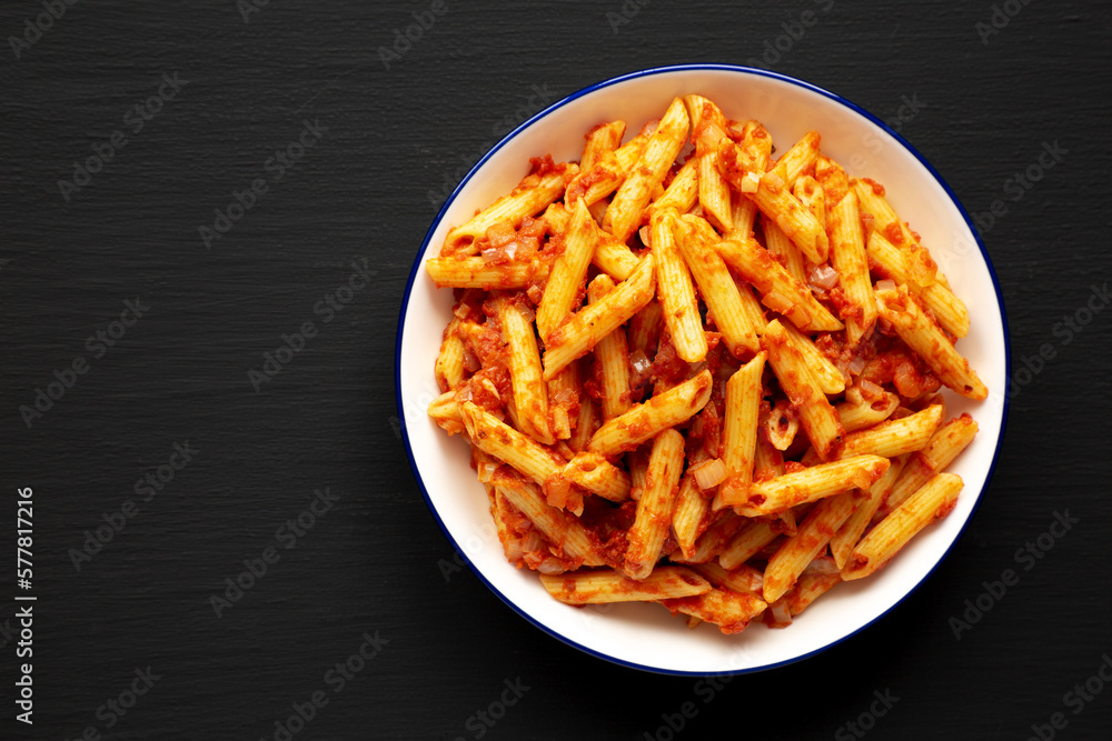 Homemade Penne With Tomato Sauce on a Plate on a black background, top view. Space for text. Homemade Penne With Tomato Sauce on a Plate on a black background, top view. Space for text.