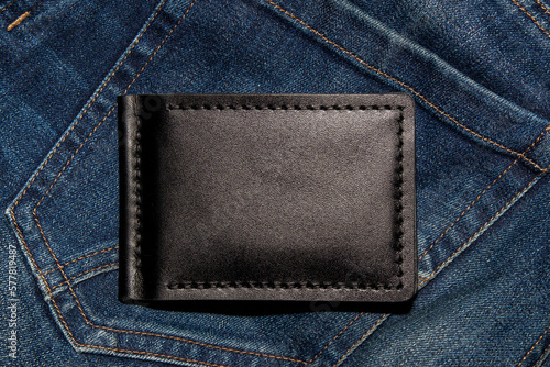 Black handmade leather wallet on blue jeans. Male background. View from above. © Oleksandr Kliuiko