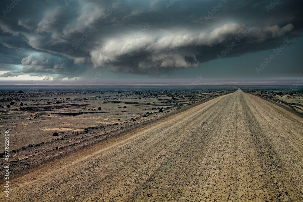 Endless gravel road in monotonous life hostile arid barren surreal gray stone and sand  atacama desert landscape, ominous dark rain storm clouds front over horizon - Chile