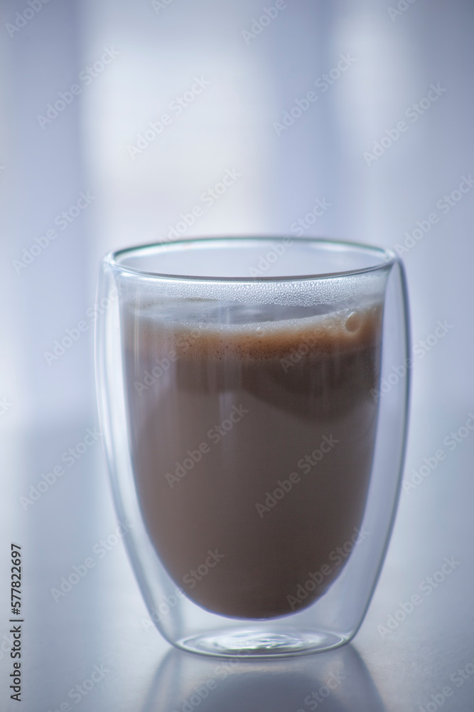 Coffee with milk in a transparent glass with a double bottom. A popular drink in an original glass. Coffee with milk in a transparent glass with a double bottom. A popular drink in an original glass.