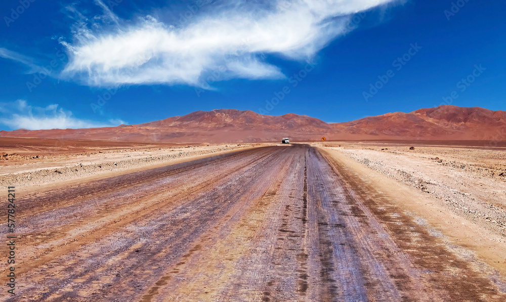 Straight empty sandy desert road through life hostile barren dry arid landscape, one single lone truck on horizon - Salar de Atacama, Chile Straight empty sandy desert road through life hostile barren dry arid landscape, one single lone truck on horizon - Salar de Atacama, Chile