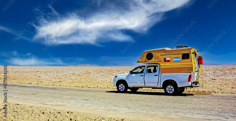 Lonely camper truck van on dirt track road in white salt flat desert, blue sky - Salar de Atacama, Chile
