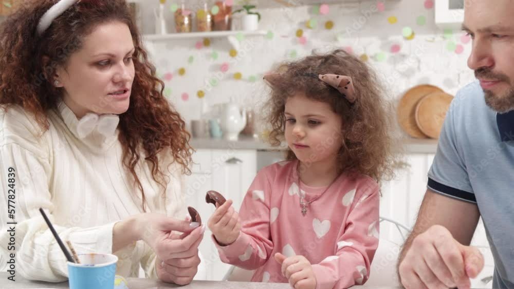 Parents having fun with cute, little daughter in their charming kitchen. Portrait of loving parents eating delicious chocolate egg with adorable toddler. High quality 4k footage Parents having fun with cute, little daughter in their charming kitchen. Portrait of loving parents eating delicious chocolate egg with adorable toddler. High quality 4k footage