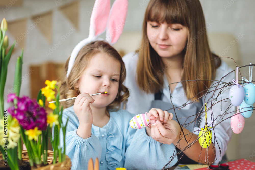 Obraz premium Beautiful mother and cute daughter are spending quality time together, making craft handmade eggs for Easter home decoration. Spring flowers, cozy holiday atmosphere , family traditions and values
