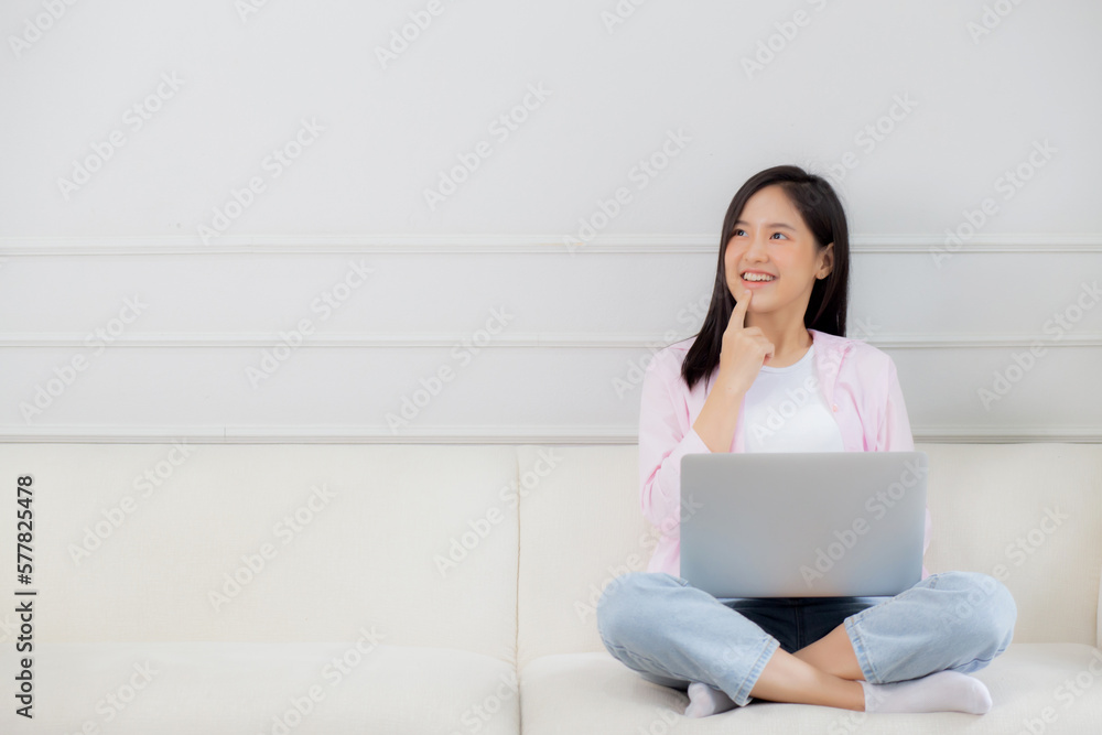 Young asian woman working on laptop computer sitting on sofa in the living room at home, female is freelance sitting on couch using notebook and doubt about decision, one person, lifestyle concept. Young asian woman working on laptop computer sitting on sofa in the living room at home, female is freelance sitting on couch using notebook and doubt about decision, one person, lifestyle concept.