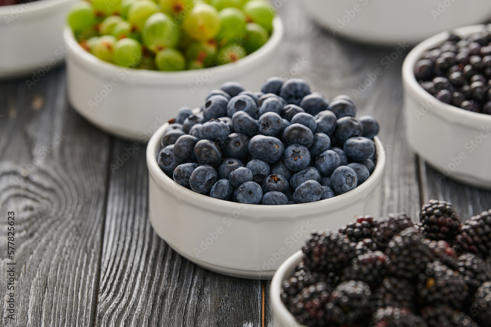 Ripe blueberries on the table in a plate, among the assortment of ripe berries, raspberries, blueberries, gooseberries, currants, shot close-up Ripe blueberries on the table in a plate, among the assortment of ripe berries, raspberries, blueberries, gooseberries, currants, shot close-up