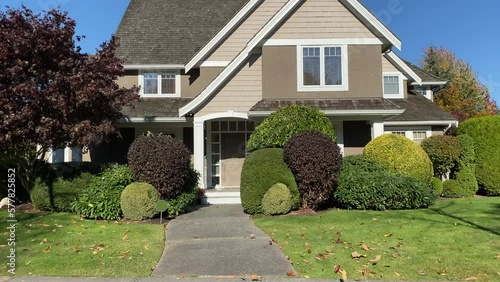 Establishing shot of two story stucco luxury house with garage door, big tree and nice Fall Foliage landscape in Vancouver, Canada, North America. Day time on Sept 2021. ProRes 422 HQ.