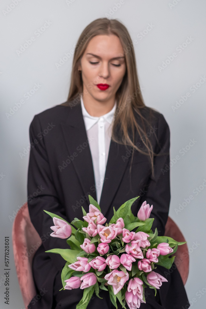 Elegant beautiful busines woman in black suit in blure. Woman holding a bouquet of pink tulips. Grey background. Elegant beautiful busines woman in black suit in blure. Woman holding a bouquet of pink tulips. Grey background.