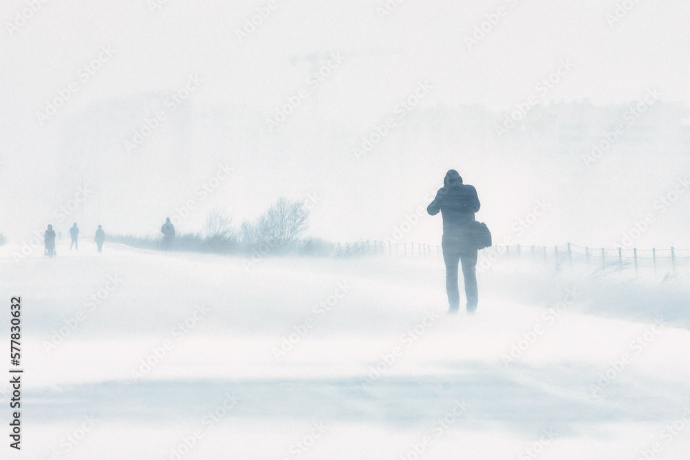 the snowstorm is cold a person has fallen into extreme living conditions is walking along the road through a blizzard in the city, the winter is cold..