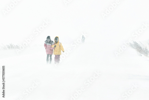 Two girls are walking along the road through a snowstorm in the city, the winter is cold..