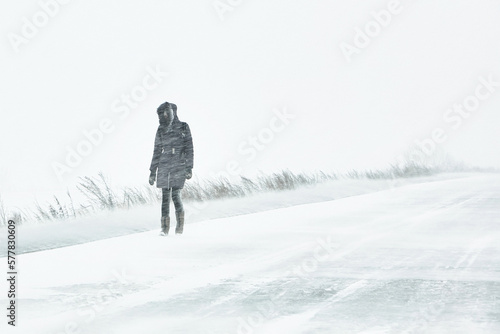 the snowstorm is cold a person has fallen into extreme living conditions is walking along the road through a blizzard in the city, the winter is cold..
