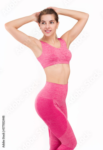 Fitness woman with a fit figure with her hands behind her head shows her figure and body.Fit woman in pink sportswear isolated on a white background showing her figure and smiling.In a pink outfit
